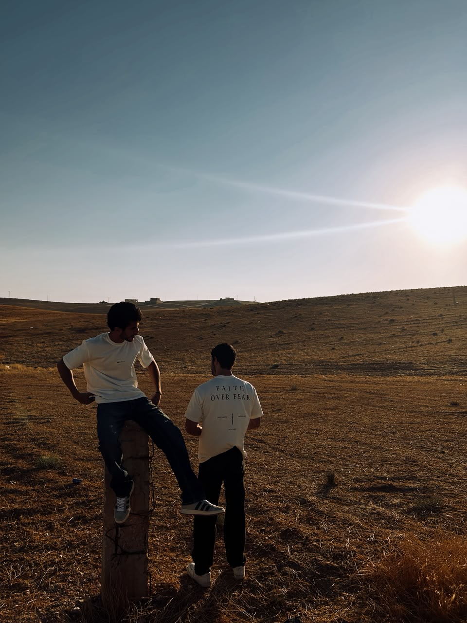 Two people in the white tee standing in an open field at dusk