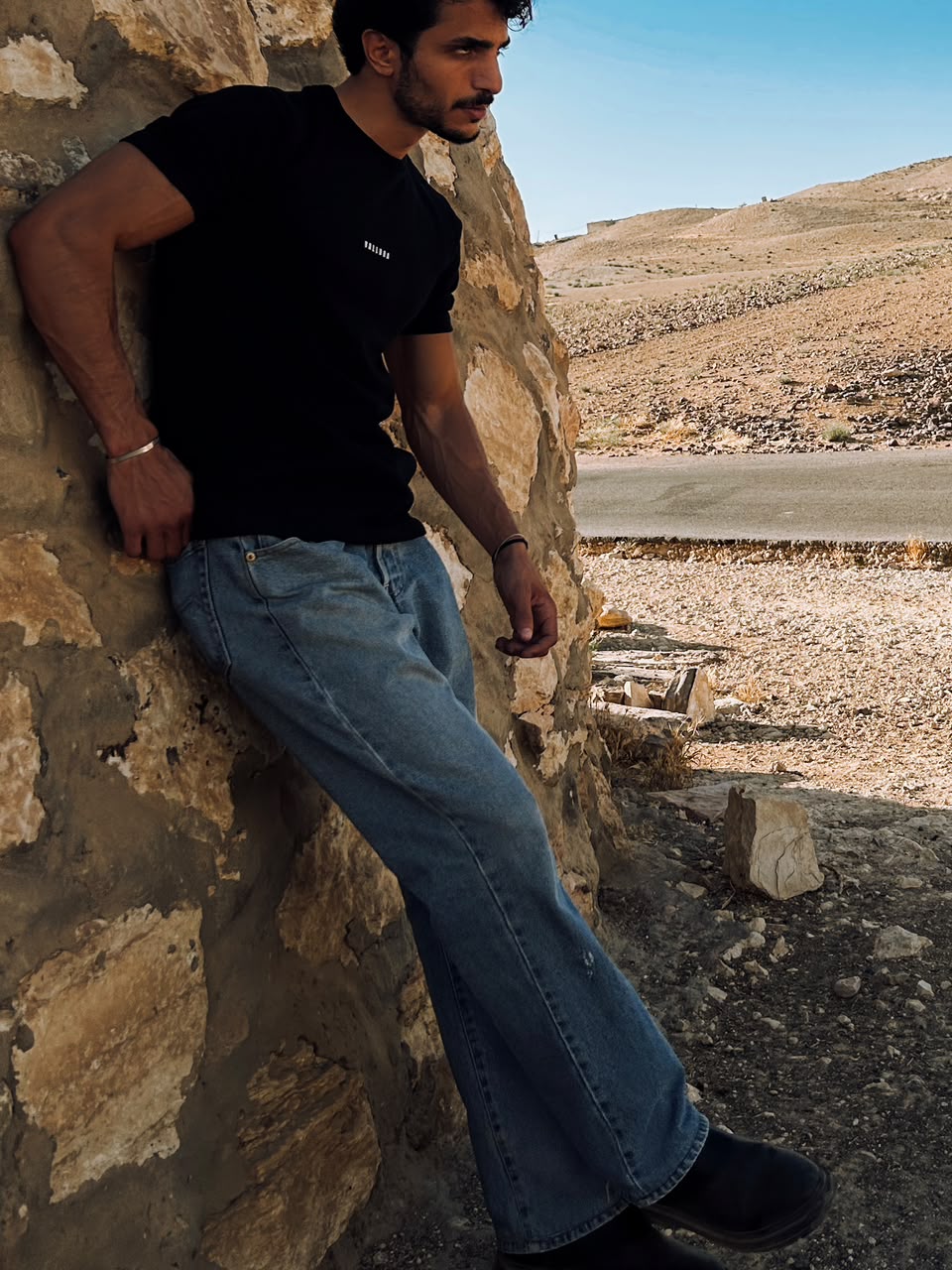 Front of the black tee with the small VALLORA chest mark, against a stone wall