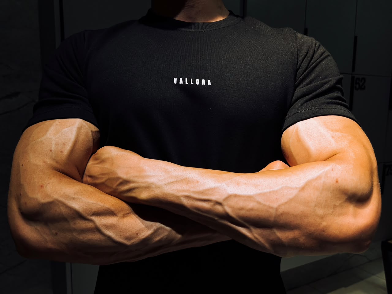 Close crop of the black tee, arms crossed, in a locker room